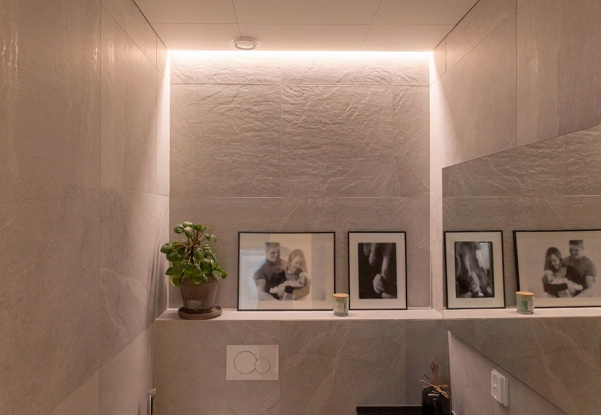 LED strip light in warm light colour temperature embedded between wall and ceiling in a toilet room.