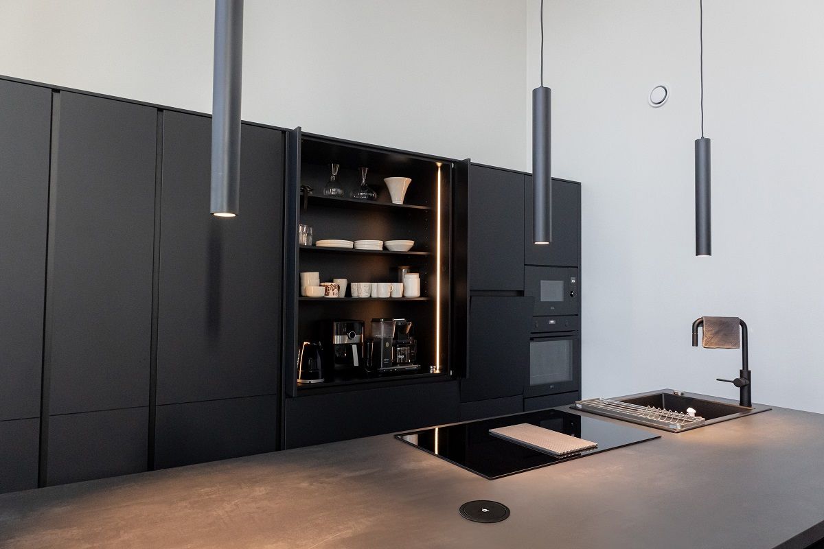 Above a black kitchen island, three black PIIPPU 2.0 pendant lights and an open breakfast cabinet with a led strip.