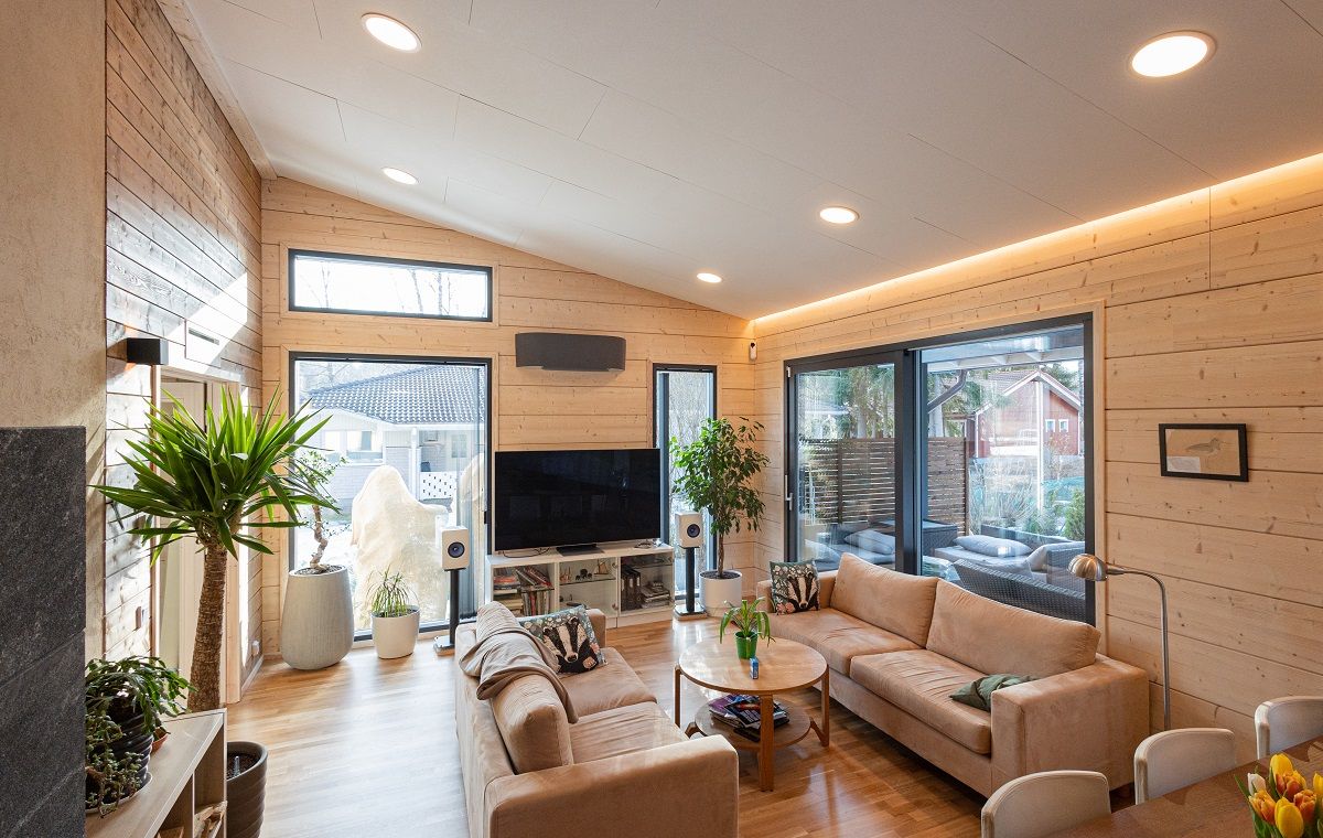 Living room with light wood surfaces and light ceiling. Recessed circular panel lights in the ceiling and a led strip at the wall/ceiling junction.