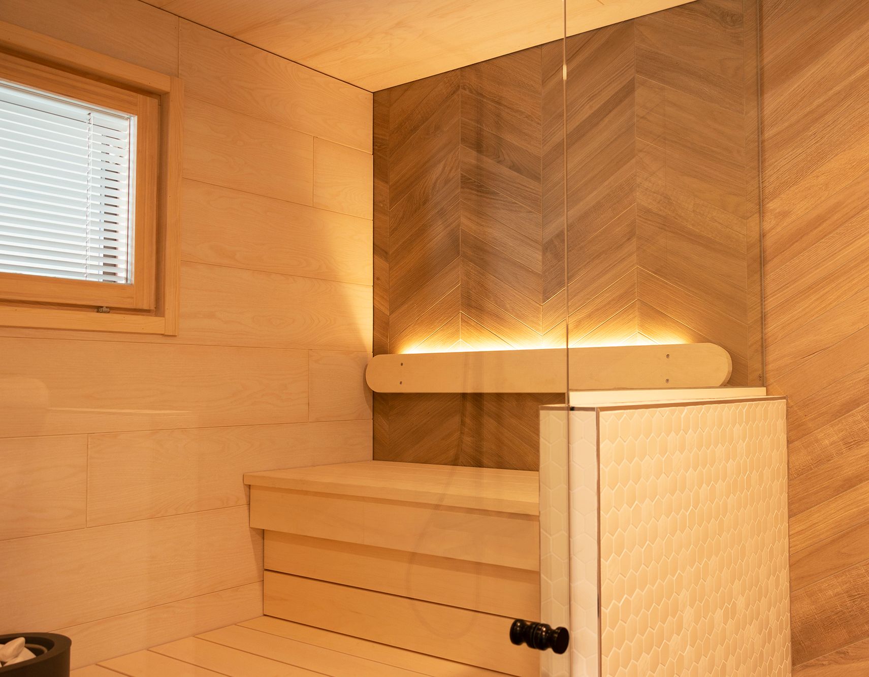 Sauna lighting implemented with a led strip on the backrest pointing upwards. The lighting in the washroom also illuminates the sauna thanks to the glass walls. Ledstore.fi