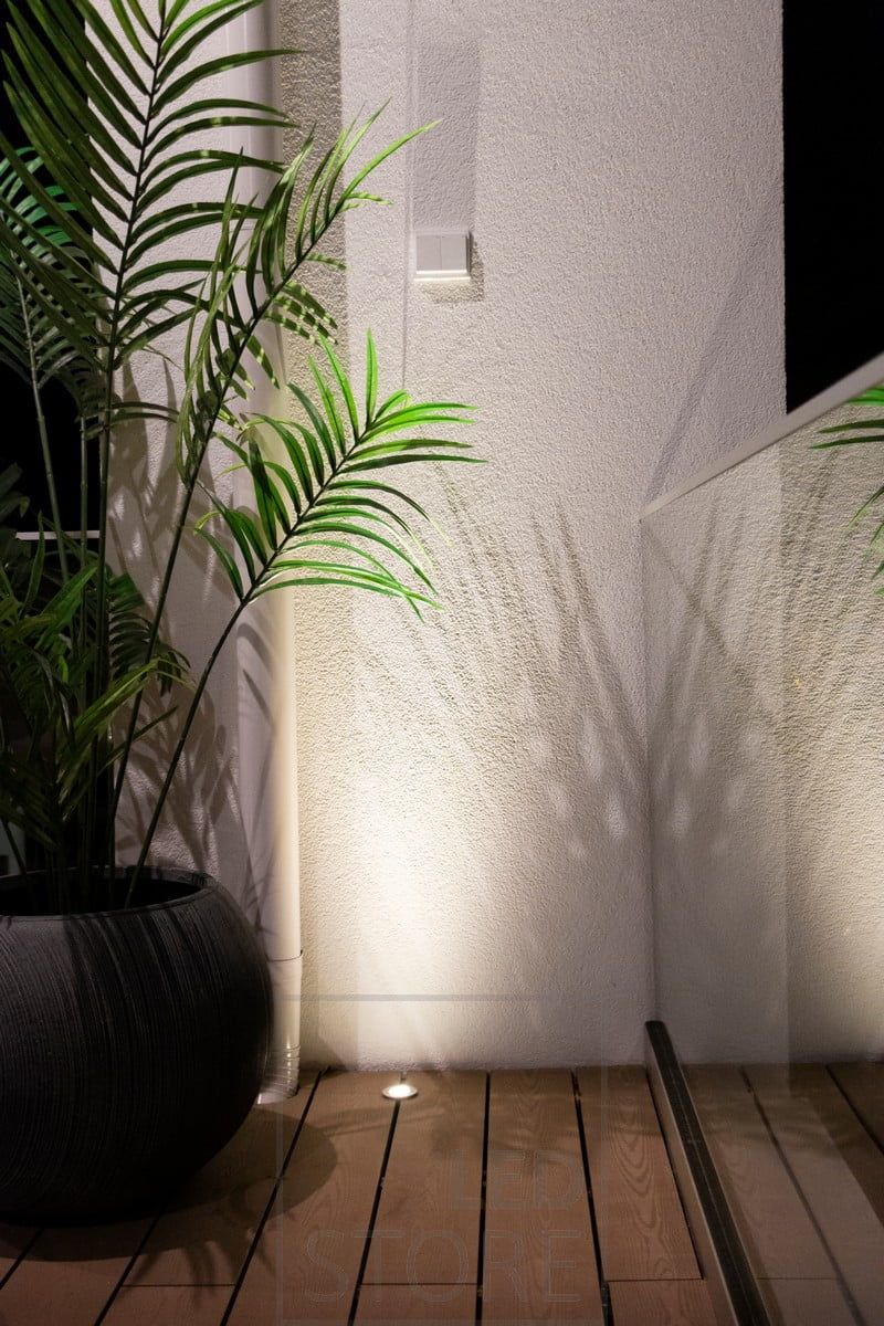 A flush-mounted patio pot close enough to the wall to provide a reflective surface for the spotlight. And thus indirect light is brought through the wall from the bottom up. Ledstore.fi