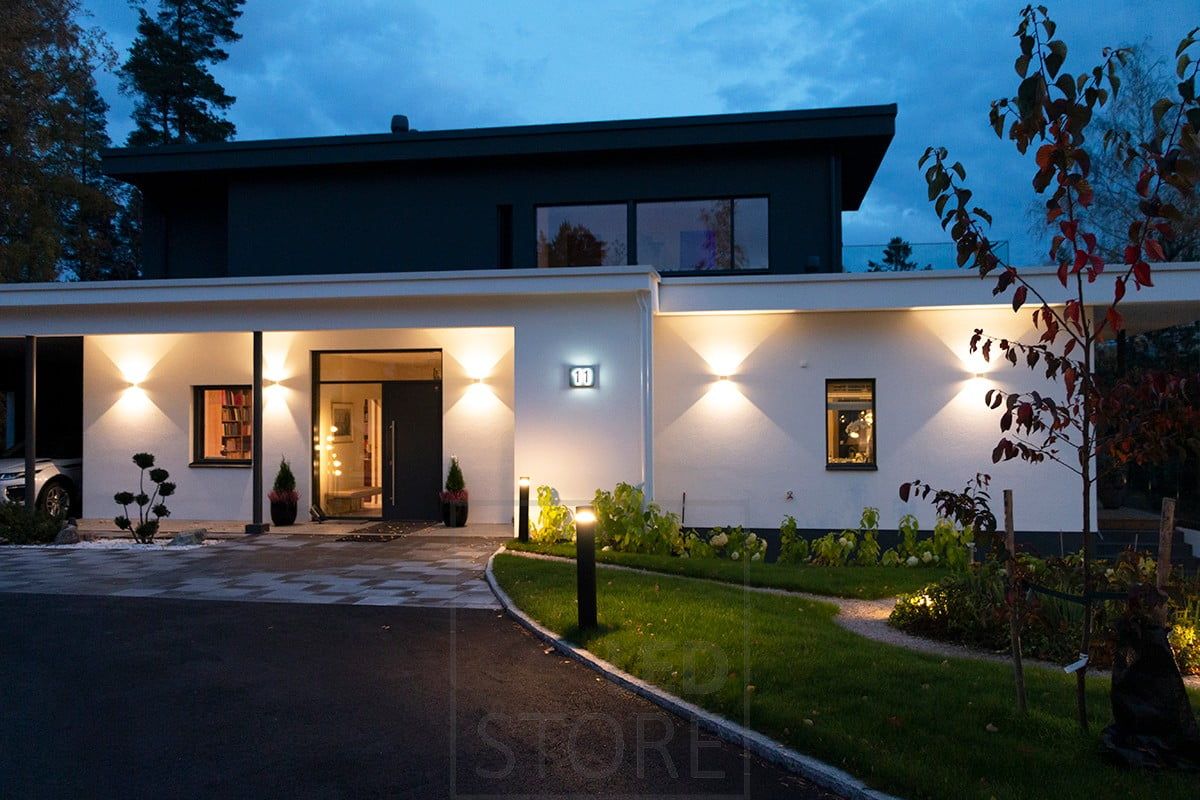 White bi-directional FUNK wall luminaire illuminating the facade and the entrance. FUNK luminaires have an adjustable light opening angle. The driveway is illuminated by pillar luminaires. Ledstore.fi