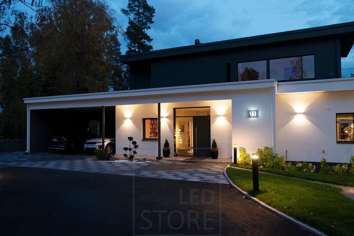 White bi-directional FUNK wall luminaire illuminating the facade and the entrance. The driveway is illuminated by pillar luminaires. Ledstore.fi