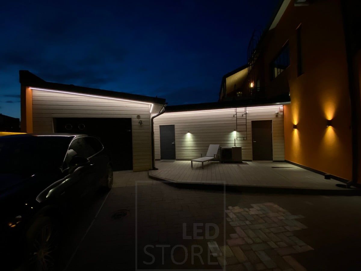 Led strip on eaves illuminating the facade of a garage and warehouse with indirect light. In addition to the eaves lighting, wall lights illuminate in one and two directions. Ledstore.fi