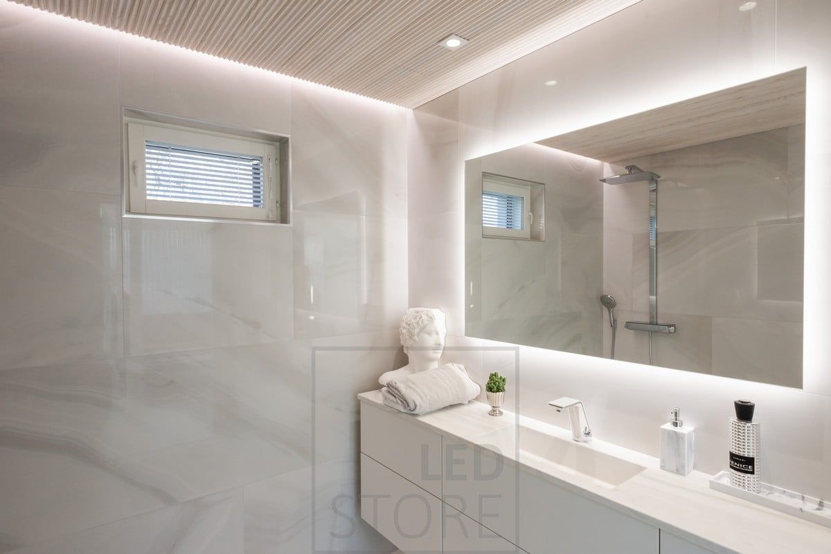 In a bathroom with a spa bath, a large, space-consuming light mirror combined with spotlights and a wall-to-ceiling LED strip.