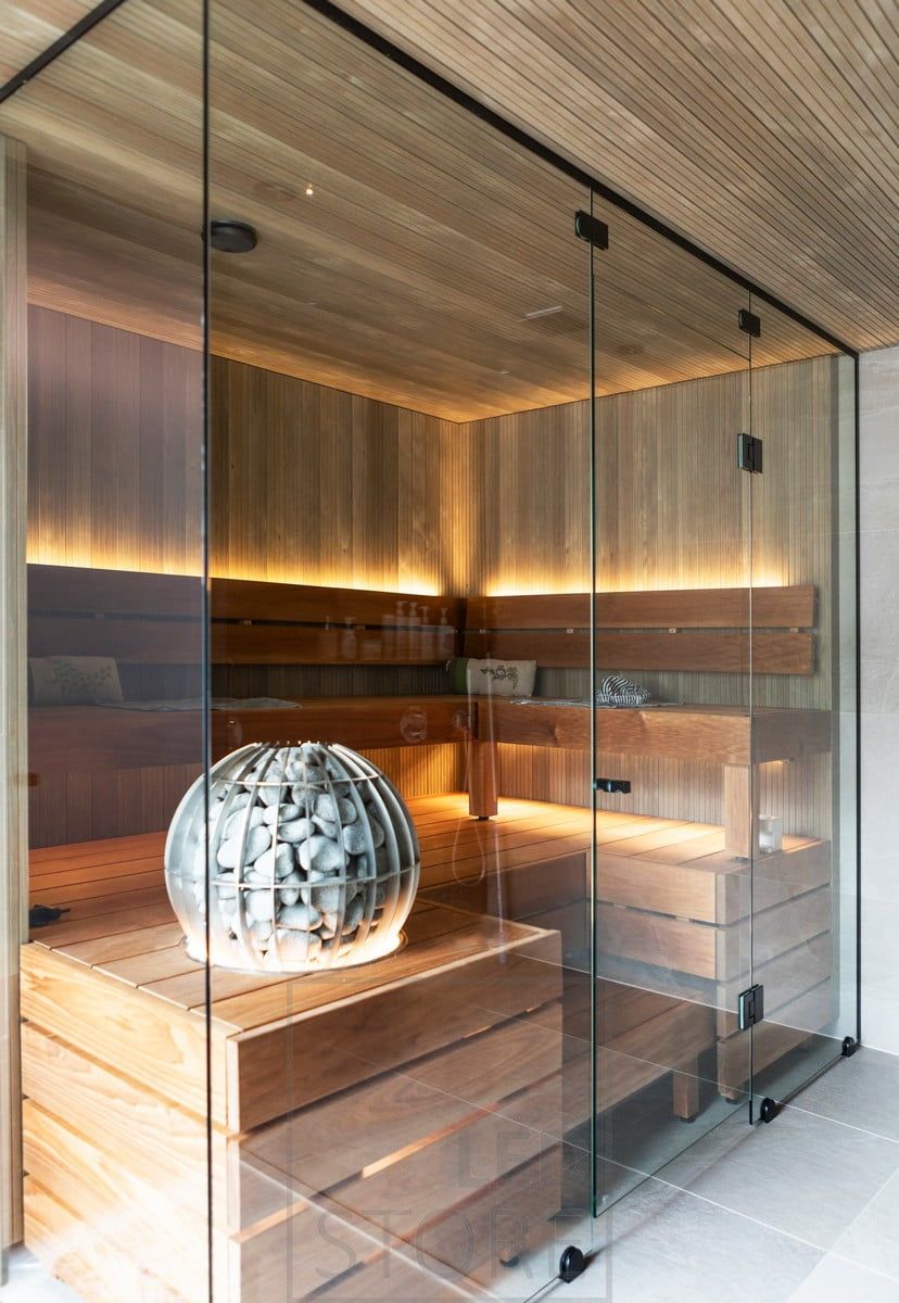 A glass-walled sauna with a LED strip light to create indirect light behind the backrest, under the ceiling and under the stove.