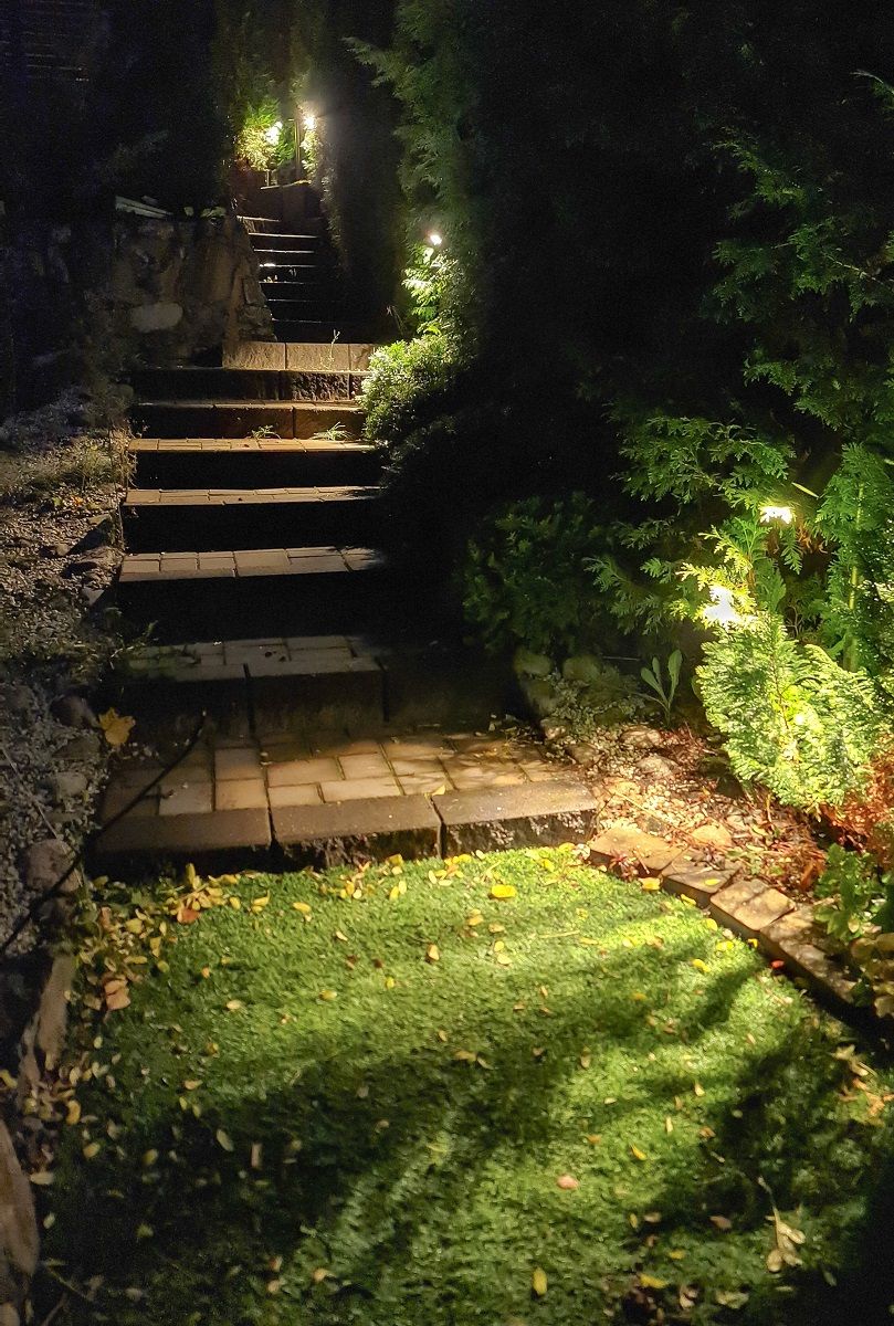 Pillar TILT 2 luminaires installed out by the stairs. The luminaire is illuminated and it is dusk outside.