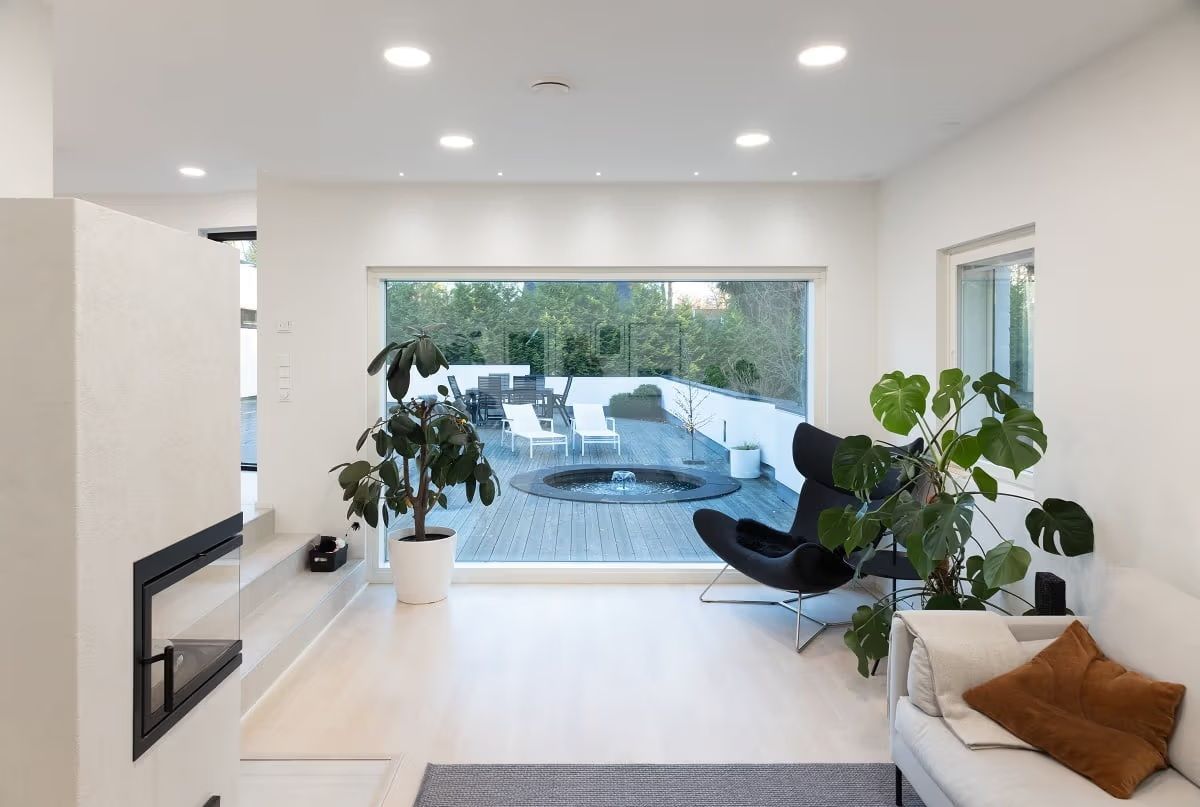 A living room with a light surface and a large window overlooking the outside. There are round LED panels on the ceiling and small spotlights in front of the window.