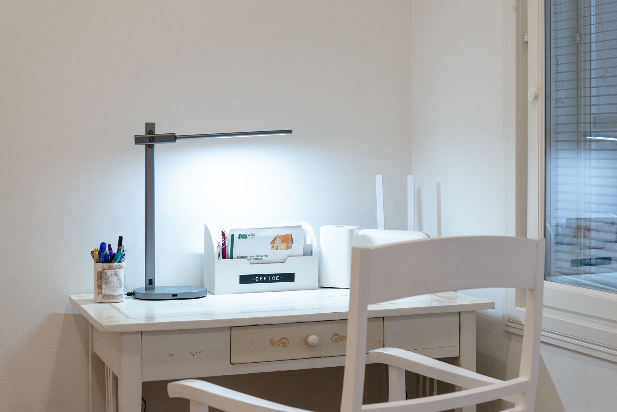 A crane table lamp illuminating a workstation. Led table lamp KURKI bedside table lamp and reading lamp in one. KURKI is a metal frame, grey, simple and elegant lamp. The KURKI led table lamp provides light directly or indirectly thanks to the freely adjustable body. Wireless and USB charging for your phone. Colour temperature adjustable and dimmable. Ledstore.fi