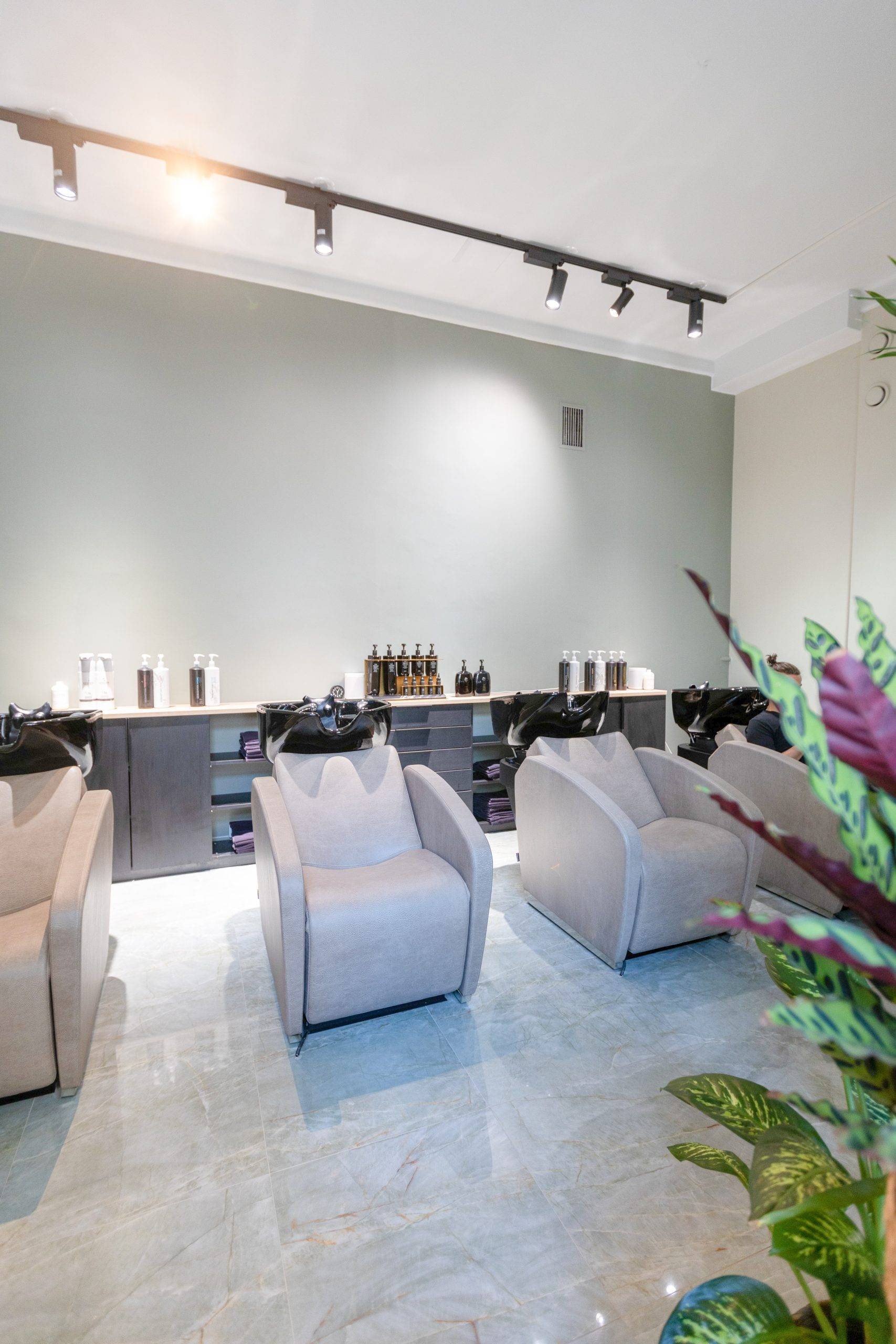 The salon’s washing station features light-colored surfaces with a black three-phase track and black FOKUS track spotlights installed on the ceiling.