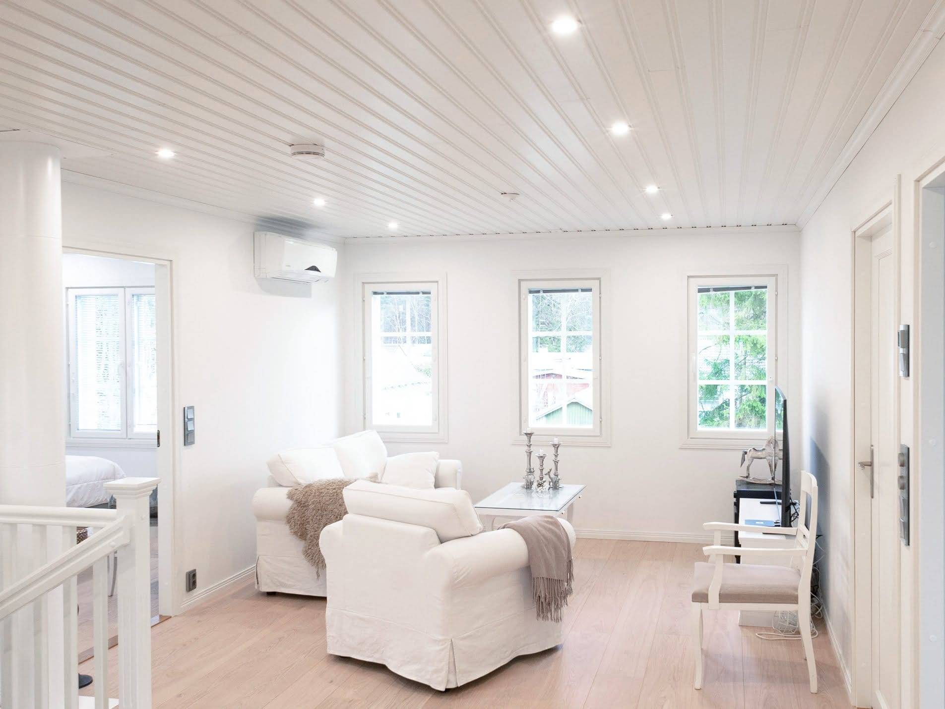Modern living room with LED lighting, white armchairs, coffee table and TV; more natural light from the large windows and accentuates the wooden floor.