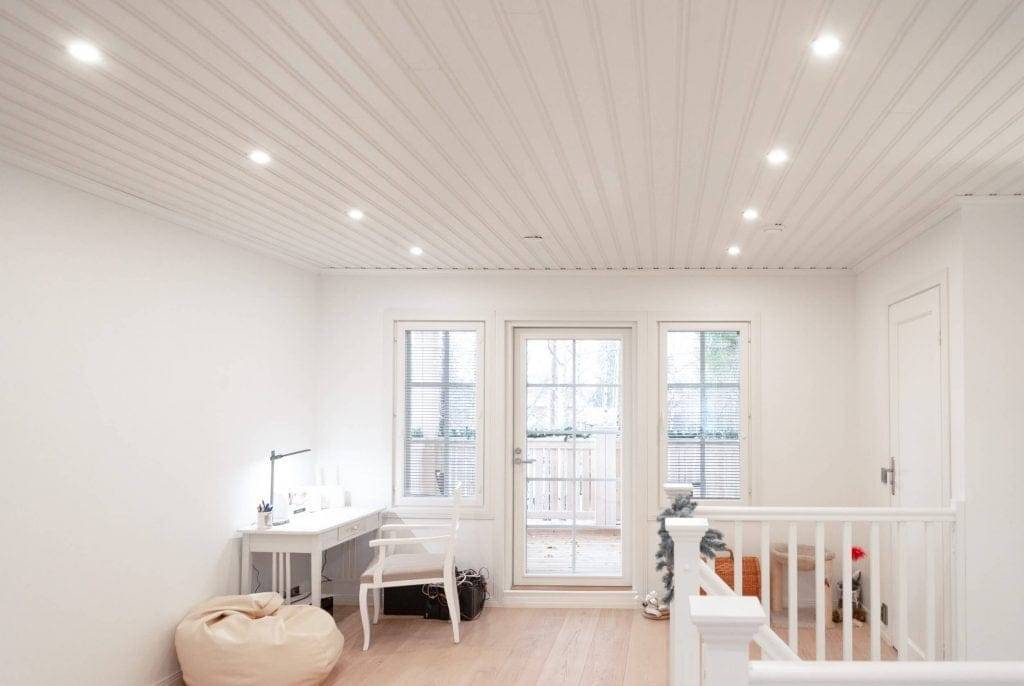 Bright room with LED recessed ceiling lights, white walls, desk, chair, bean bag, glass doors to balcony; staircase with white railing on the right.