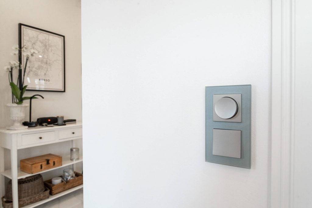 Modern LED light switch with two buttons on a white wall; white console with potted orchid and framed map in a minimalist room.