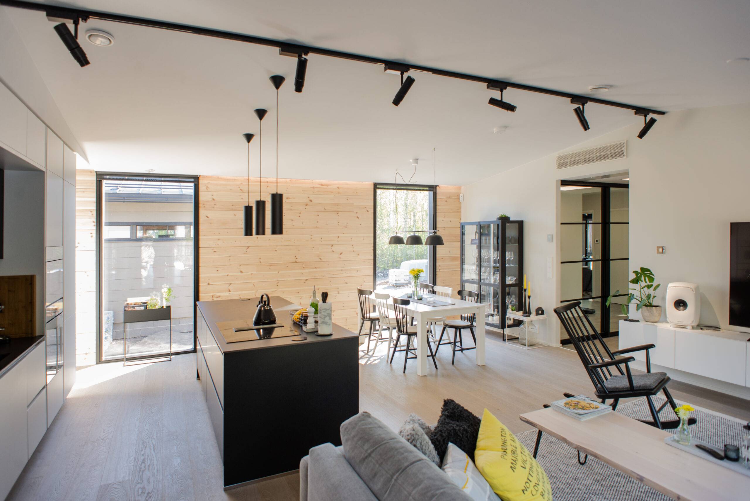 Modern open-plan kitchen and living room with wooden details and black furniture for a stylish look. High-quality interior lighting from LedStore.fi creates a great atmosphere, and large windows let in natural light.
