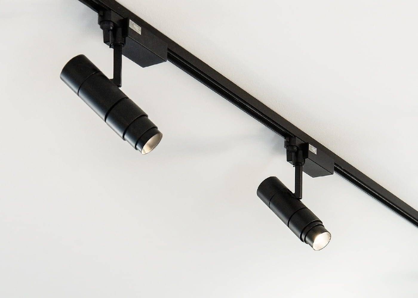 Two black LED track lights on a white ceiling, providing efficient, focused downward illumination to enhance the room's ambiance. Perfect modern lighting.
