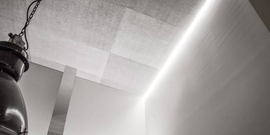 Modern minimalist interior with gray ceiling, built-in LED lighting at edges; industrial-style light fixture hangs from chain, smooth light walls