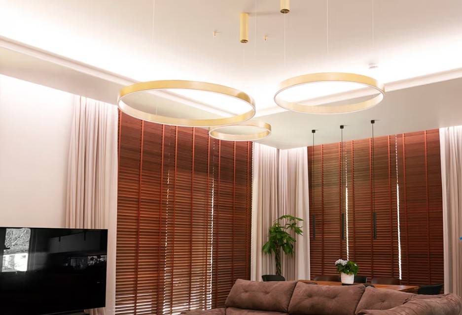 The modern family living room in Kaitamäki, Espoo, features a stunning LedStore.fi lighting scheme: large, gold-coloured ring lights create a luxurious atmosphere alongside matching brown blinds and a cosy sofa. Finished off with a stylish TV and lush greenery - this is the kind of lighting that makes your home feel cosy and impressive!