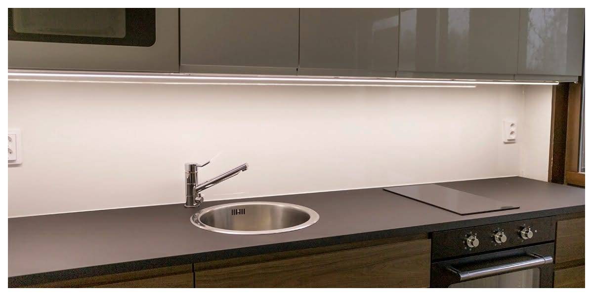 Modern kitchen with black countertop, stainless steel sink, chrome faucet, stovetop, oven, and LED-lit upper cabinets for stylish illumination.