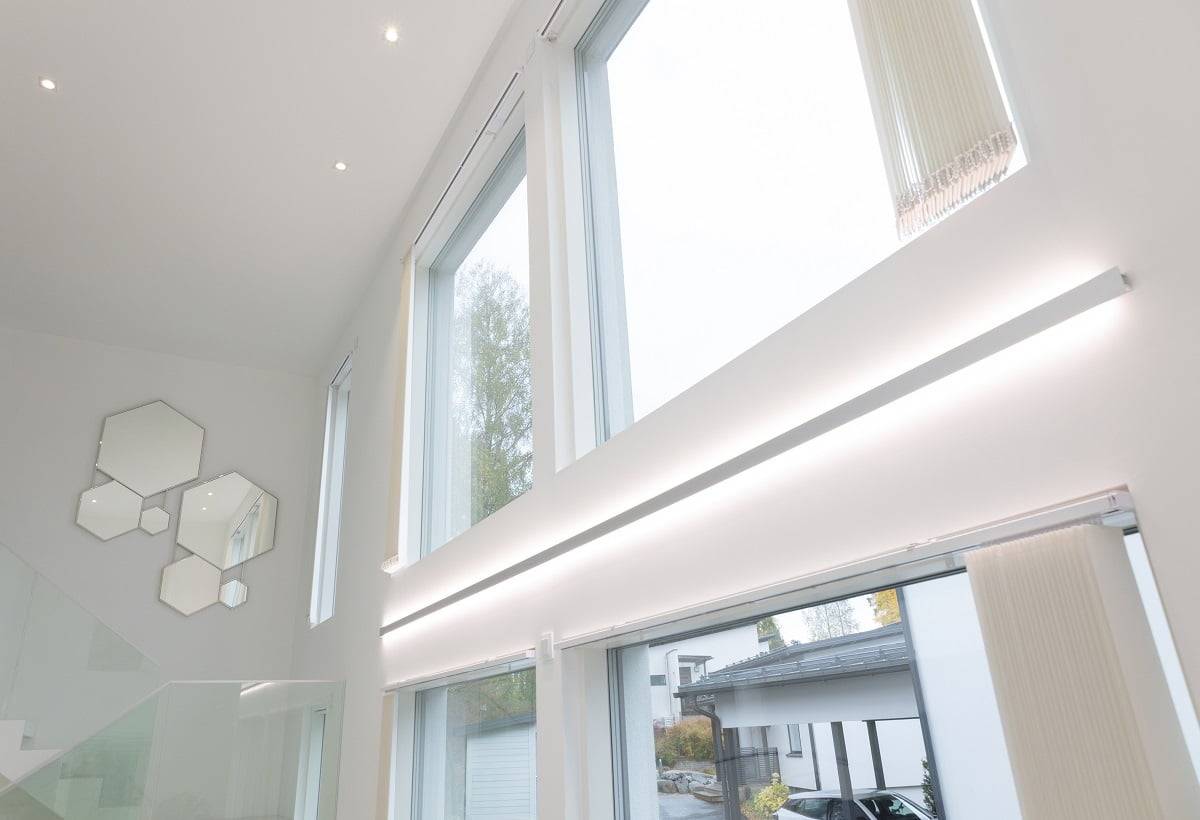 LedStore.fi online store product description: the modern interior features stunning large and high windows, problems with stylish LED lighting. This lighting allows natural light to flood in. On the white walls there is an artistically arranged set of hexagonal mirrors near the staircase with a glass balustrade. Outside, the driveway is lined with parked cars, completing the modern style.