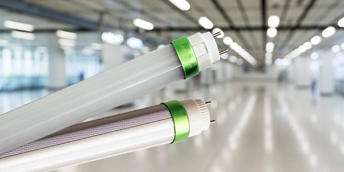 Close-up of two horizontal fluorescent LED light tubes with green accents in a bright room, enhancing ambiance on reflective flooring.