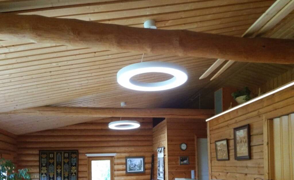 LedStore.fi esittelee modernin LED-valaistusratkaisun rustiikkiin puusisustukseen, jossa on vino katto ja tukevia hirsiä. Kattovalaisimina toimivat kaksi tyylikästä LED-ympyrävalaisinta luovat tunnelmallisen valaistuksen. Seinillä roikkuvat kauniisti kehystetyt kuvat ja elävä tekstiili tuovat lisälämmön tänne kodikkaaseen tilaan.