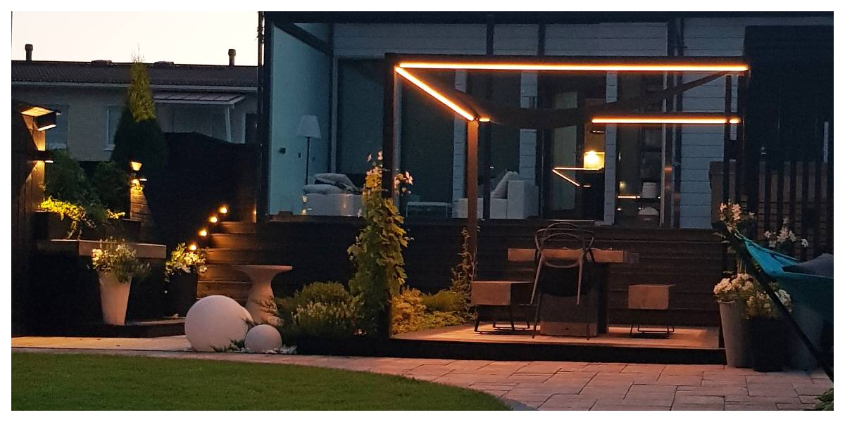 A modern backyard patio with a pergola and stunning LED mood lighting. A wooden staircase and atmospheric potted plants complete the look. This setup, located in the yard of a modern home, offers the perfect setting for evening moments, all enhanced by LedStore.fi's high-quality LED lighting.