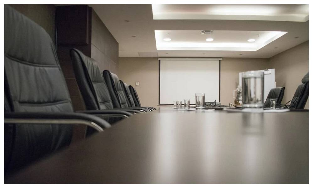 Conference room with large dark table and chairs. There are several panel and spot lights in the ceiling.  