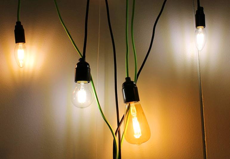 The black and green wires of four stylish LED lamps hang against a light wall, for a modern interior.