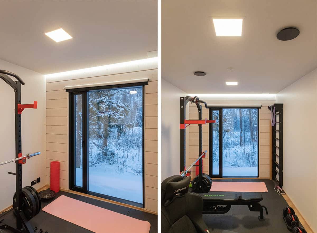 A small gym with a large window to the outside, two small panel lights on the ceiling and a led strip above the window.