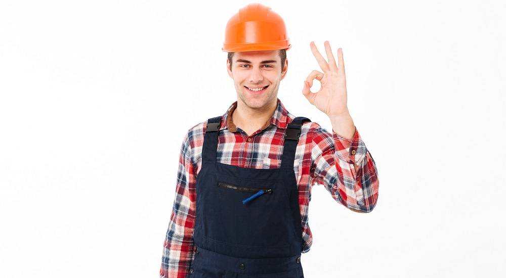 Portrait of a cheerful young male builder showing thumbs up gesture while standing and looking at camera isolated over white background.