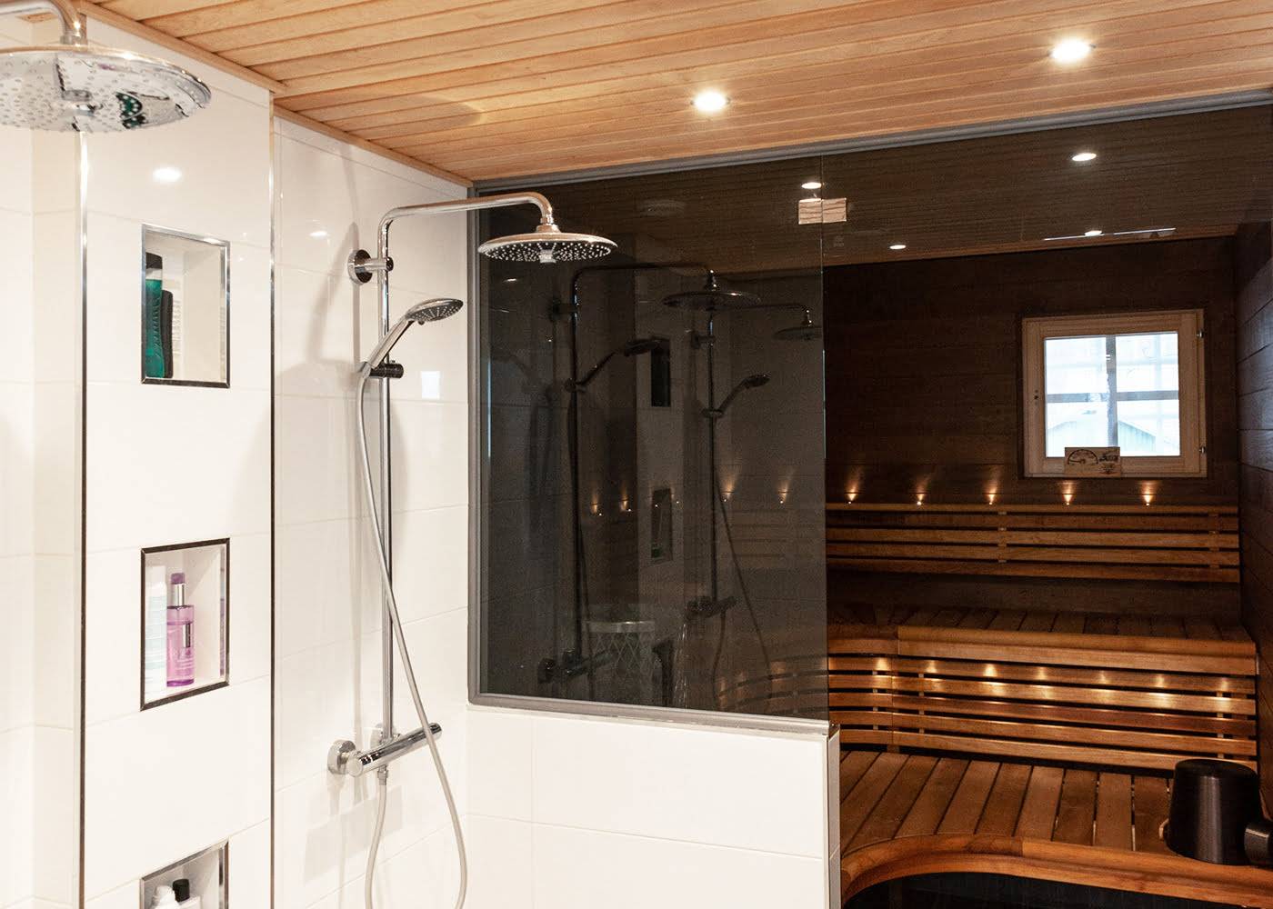 Modern bathroom with two rain showers, glass wall, built-in toiletries shelf, adjoining wooden sauna, atmospheric window lighting and LED lighting.