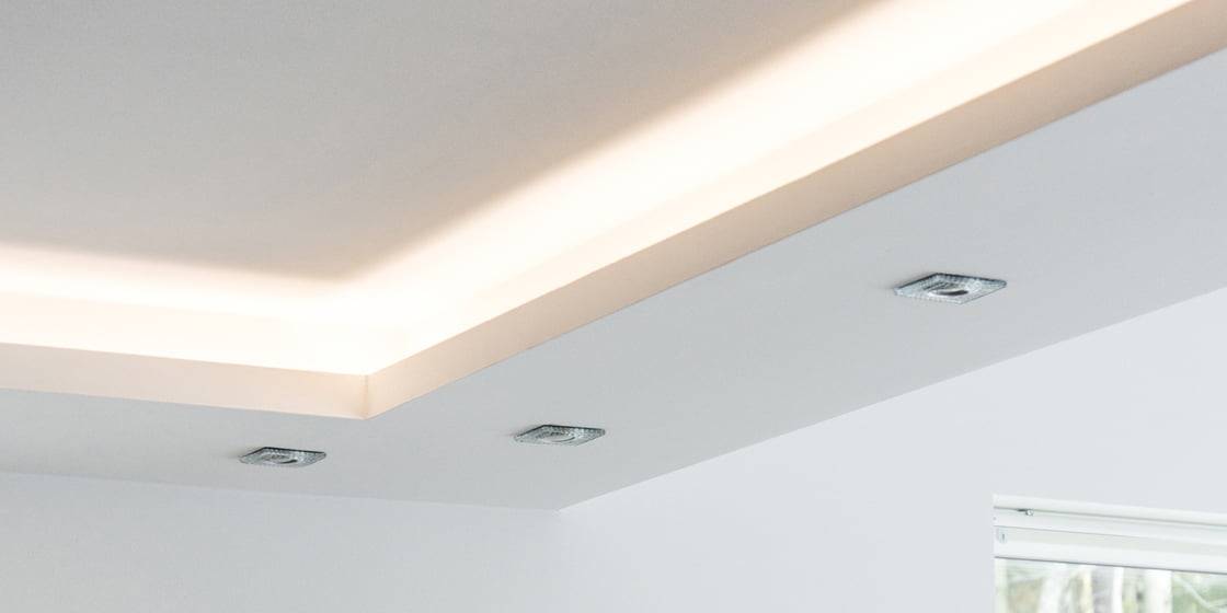Modern ceiling with recessed LED lighting, indirect cove lights, clean white surface, soft LED glow enhancing design; window visible bottom right.