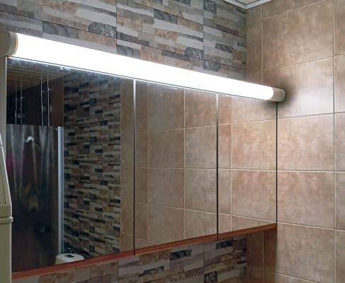 An illuminated fluorescent light fixture housing above a mirror cabinet.