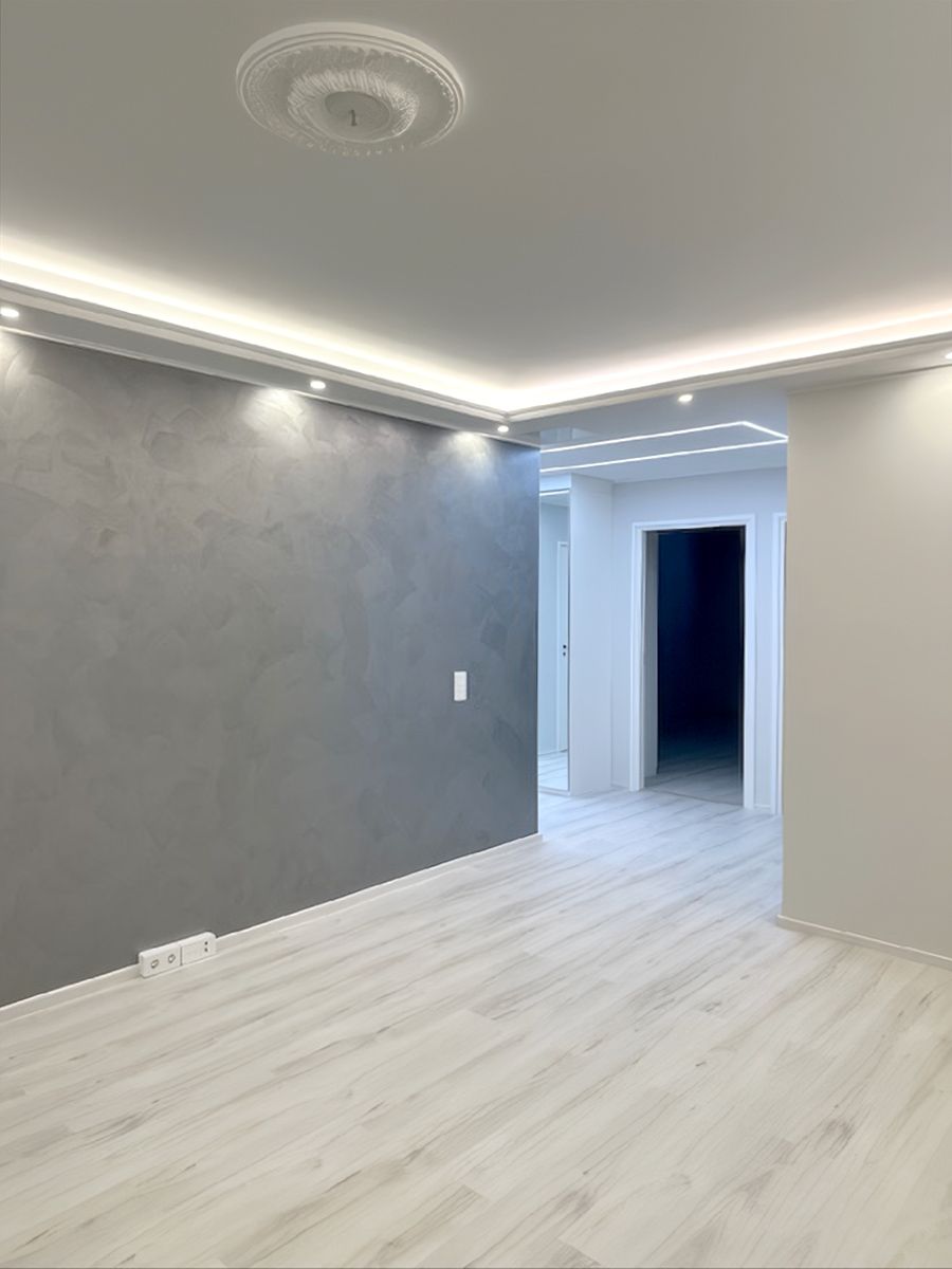 A ceiling structure with a drop ceiling on the edges of the room, with indirect LED strip lighting and downward spotlights.